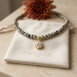 Dalmatian Jasper and Zircon Teardrop Necklace on the cream simple pouch with a blurred autumn flower