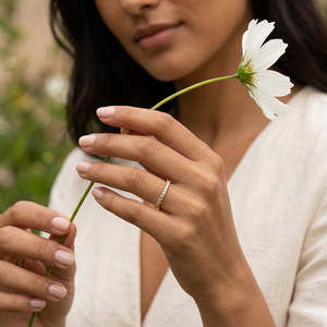 Woman holding a white flower while wearing the thin gold ring